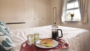 Ein ordentlich bezogenes Bett mit einem Tablett mit Frühstücksangeboten, darunter Croissants, eine Kaffeemaschine und zwei Tassen.