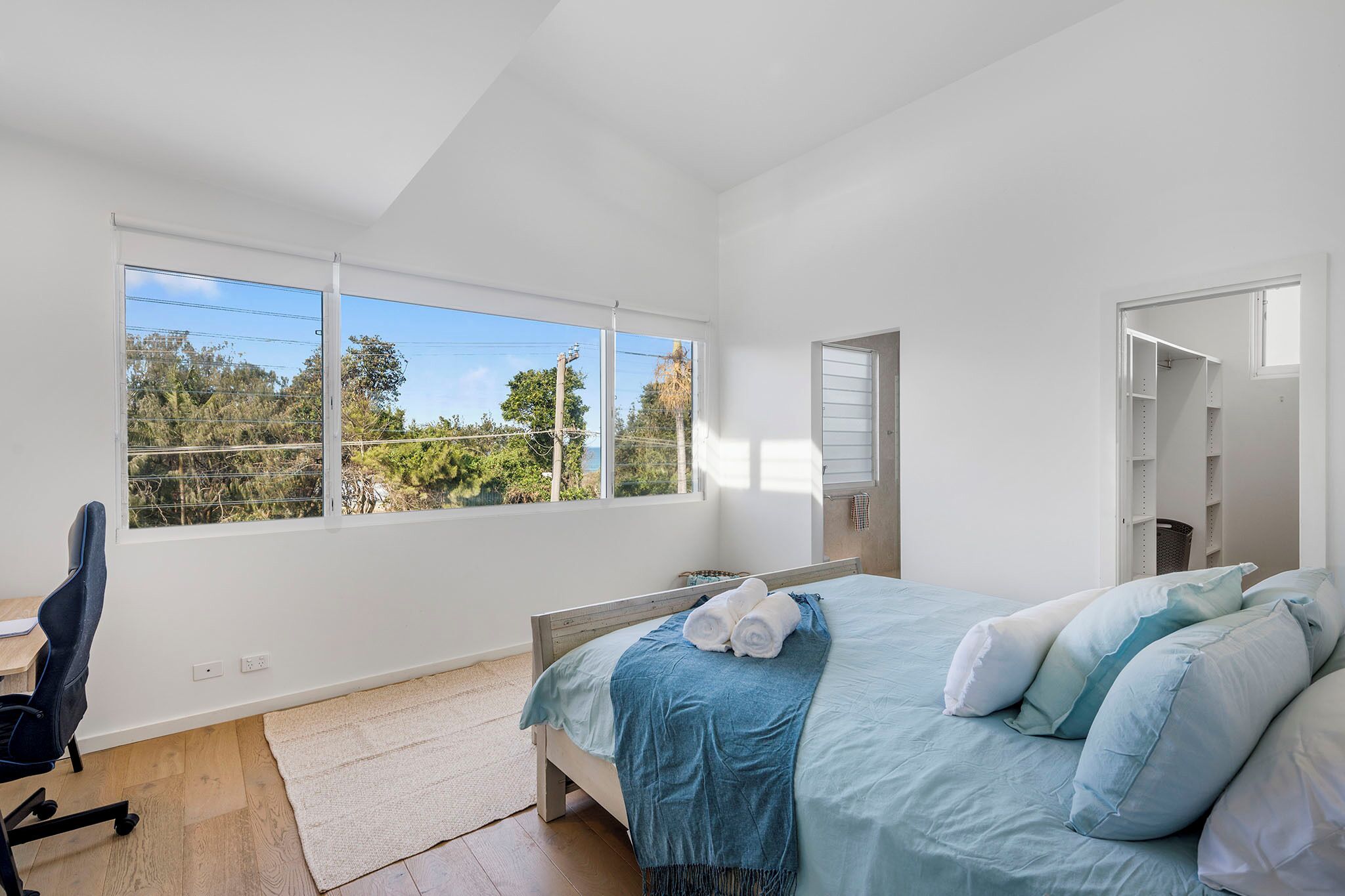Une chambre à coucher avec un lit, un bureau et une fenêtre donnant sur des arbres et des lignes électriques.