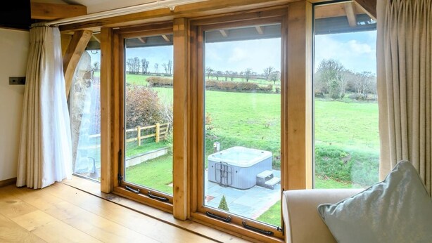 A room with large windows, wooden beams, and a hot tub visible outside. - 1 Bed in South Molton (oc-59339) (East Knowstone)