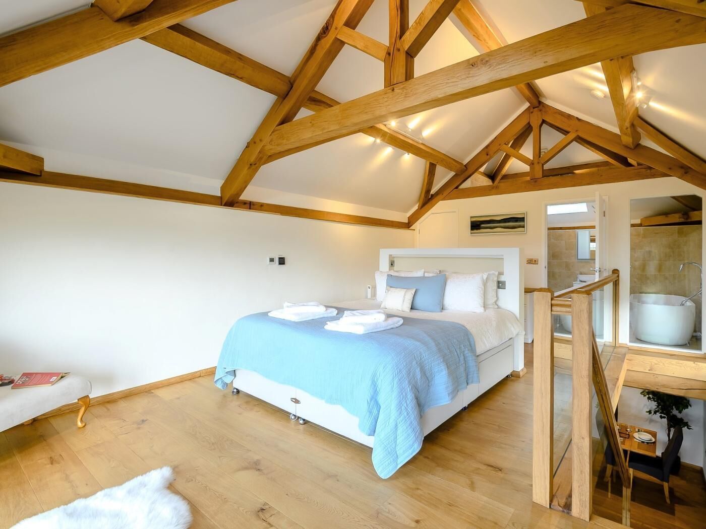 Une chambre à coucher avec un lit, des poutres en bois, une table de chevet et une salle de bain avec une baignoire.