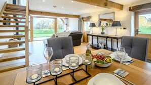 A dining area with a table set for four, a wooden staircase, and a large window offering a view of the outdoors. - 1 Bed in South Molton (oc-59339) (East Knowstone)