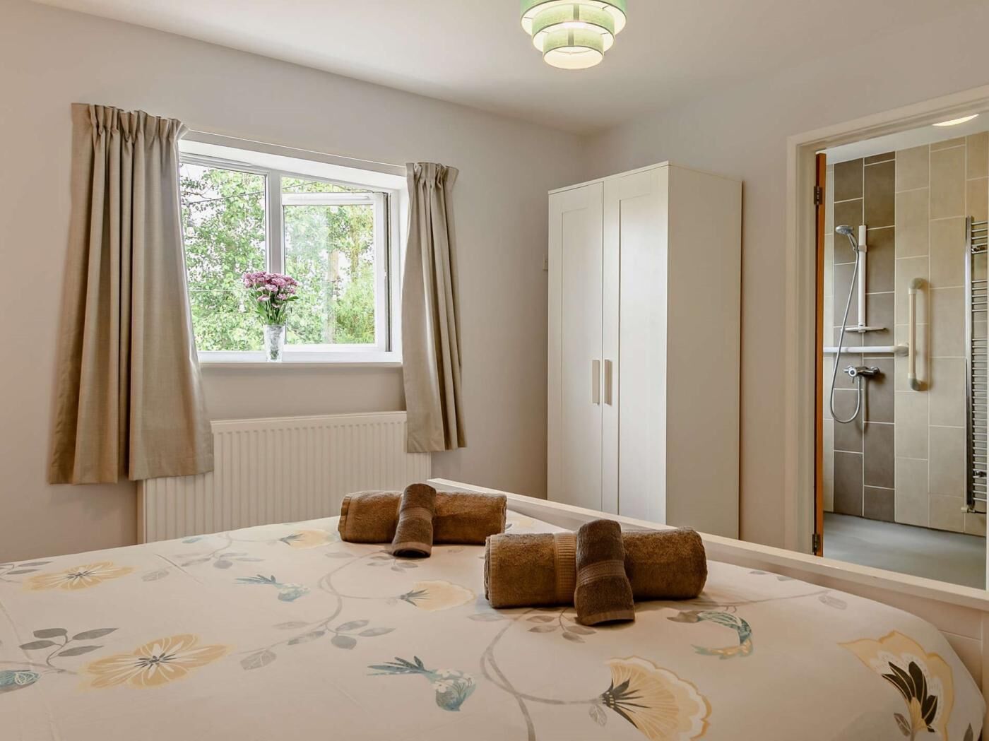 A bedroom with a bed, a window with curtains, a wardrobe, and a shower area.