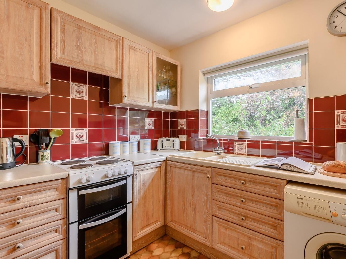 Une cuisine avec des meubles en bois, une cuisinière, un lave-vaisselle et une fenêtre donnant sur un paysage verdoyant.