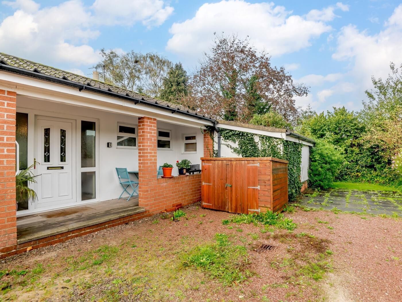 A house with a covered porch, a wooden shed, and a garden area.
