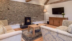 Een gezellige woonkamer met een stenen muur, houten balken, een open haard, een televisie en comfortabele zitmogelijkheden.