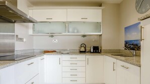Una cocina con armarios blancos, una campana de acero inoxidable, un hervidor, un tostador y un reloj en la pared.