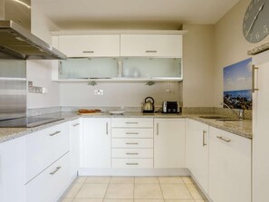 Eine Küche mit weißen Schränken, einer Edelstahl-Dunstabzugshaube, einem Wasserkocher, einem Toaster und einer Uhr an der Wand.
