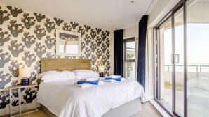 Habitación de hotel con una cama grande, una mesita de noche, un ventanal con vistas y una pared con estampado de cactus.