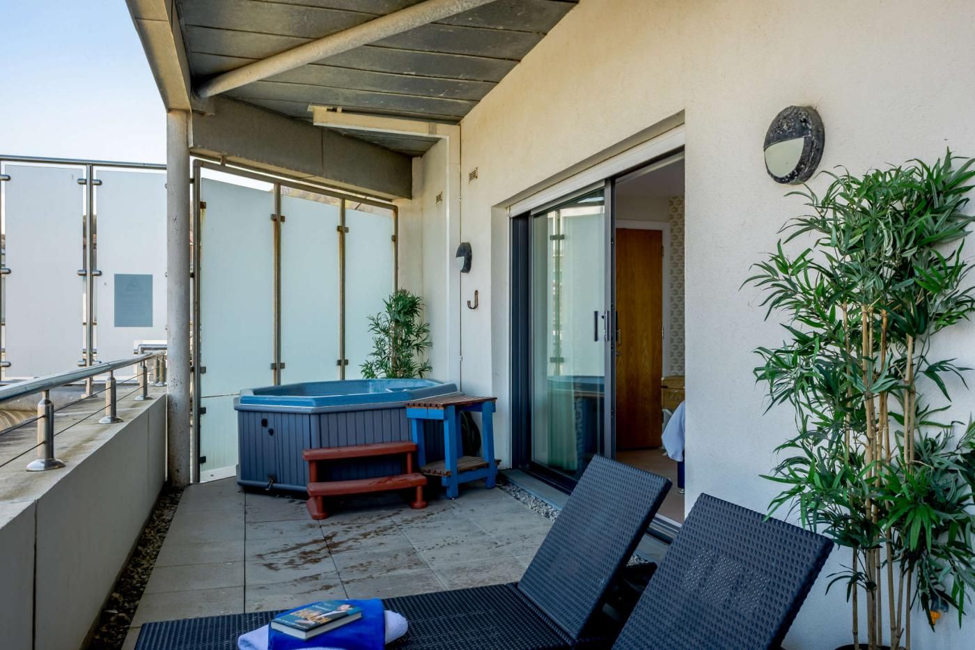 A balcony with a hot tub, seating, and a potted plant.