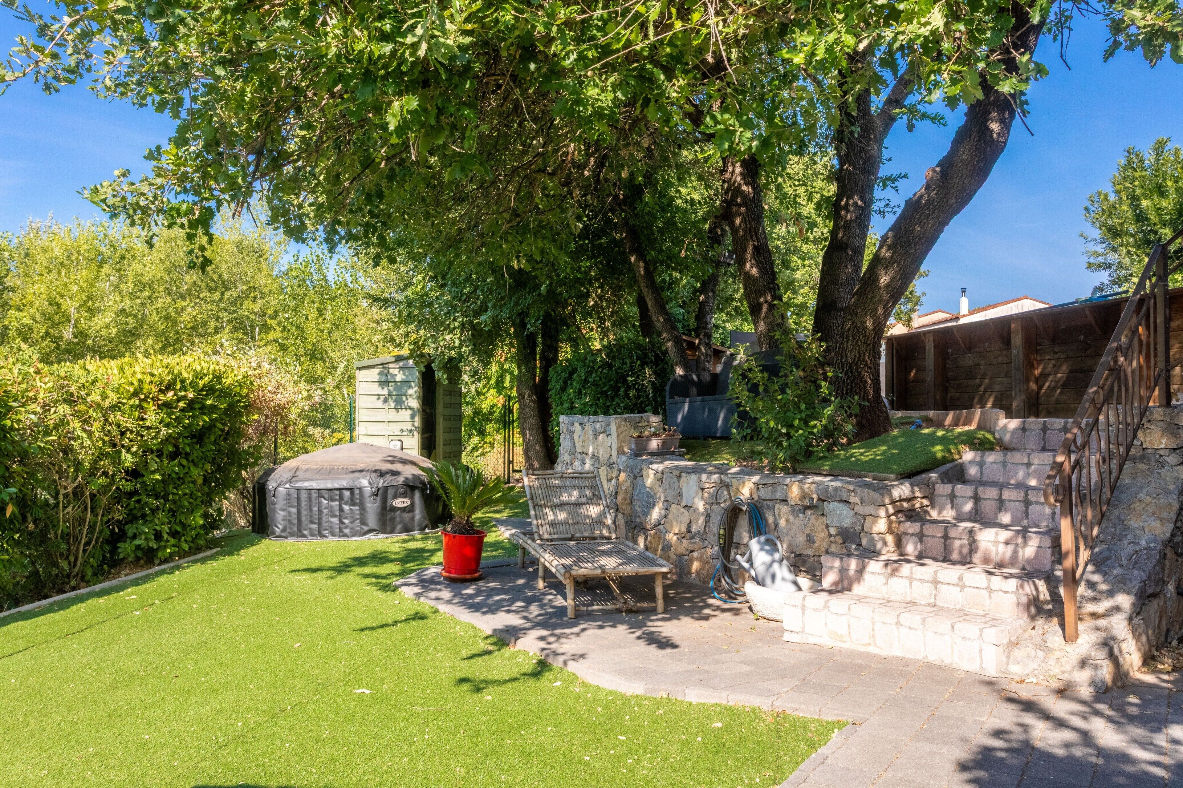 A backyard with a stone wall, a wooden bench, and a covered outdoor seating area.