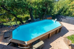 A rectangular swimming pool with a wooden deck surrounding it, set in a landscaped backyard with trees and a fence.