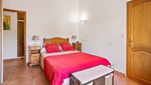 Un dormitori amb un llit, taules de nit, una estació de nit, una porta de fusta i una paret amb un disseny texturat.