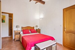 A bedroom with a bed, bedside tables, a nightstand, a wooden door, and a wall with a textured pattern.