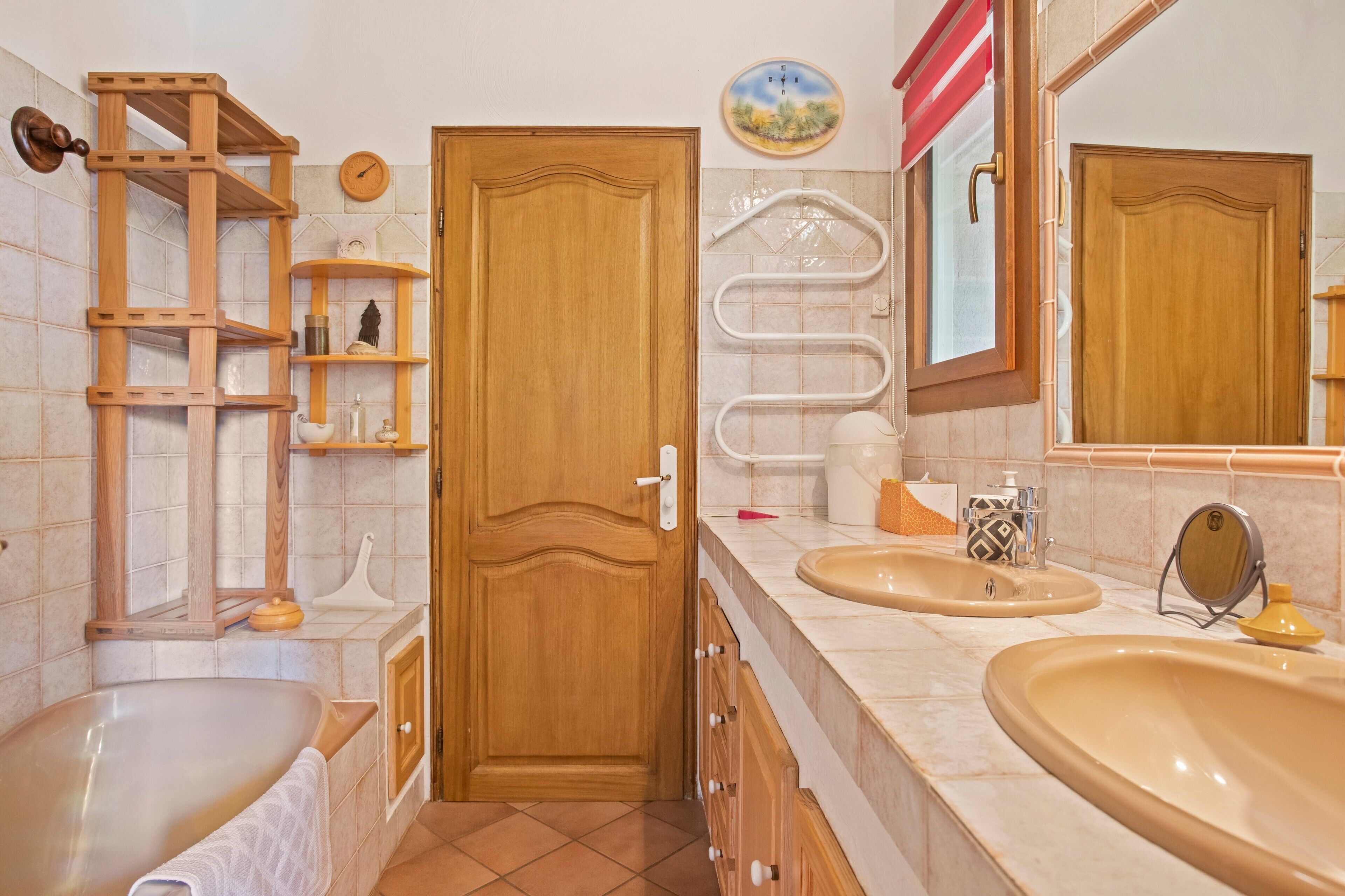 Une salle de bain avec une porte en bois, deux lavabos, une baignoire et un porte-serviettes.