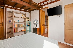 A bedroom with a bed, a bookshelf, a fan, and a TV mounted on the wall.