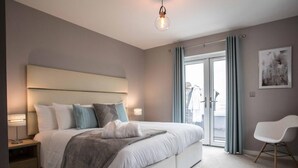 Ein modernes Hotelzimmer mit einem großen Bett, Nachttischlampen, einem Sessel und Blick ins Freie.
