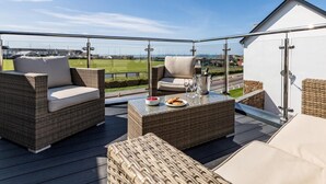 Eine Dachterrasse mit Korbmöbeln, einem Glastisch und Blick auf ein Sportfeld.