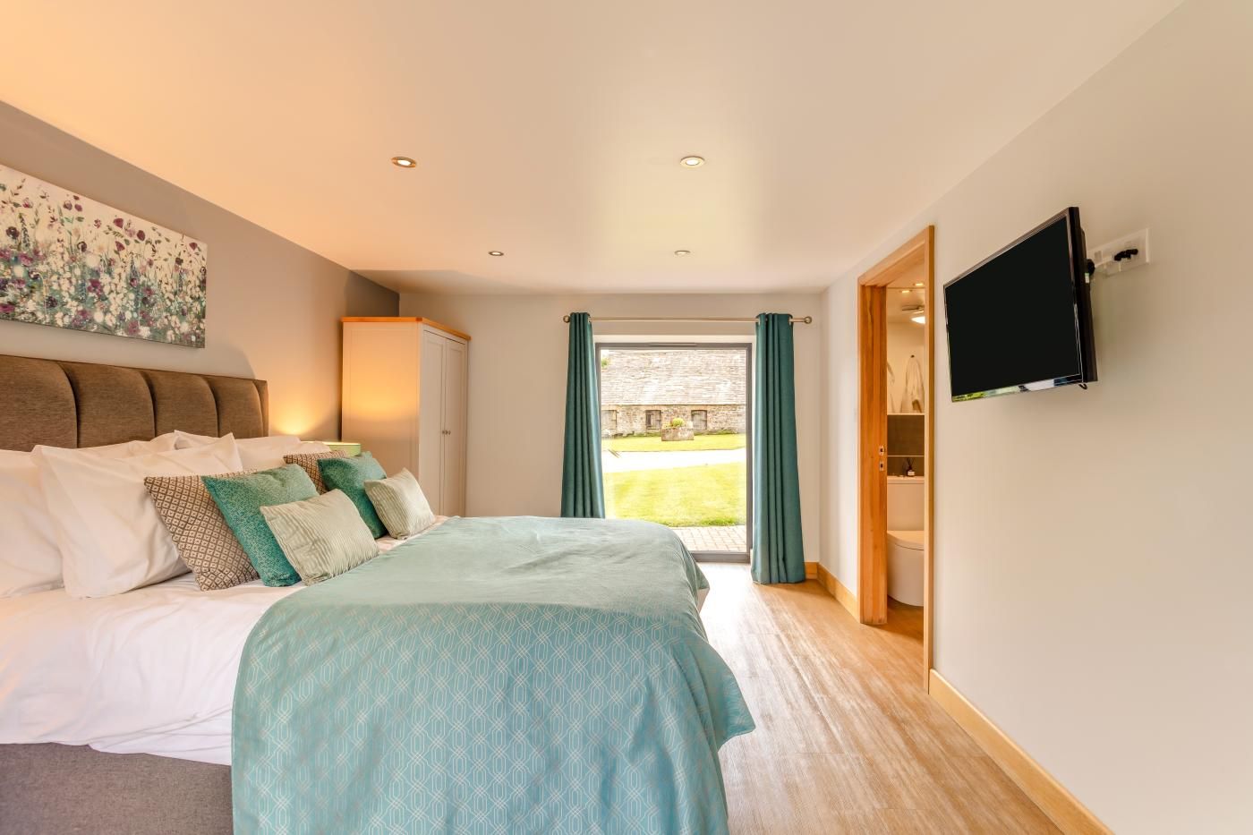 A bedroom with a bed, a television, and a view of the outdoors.
