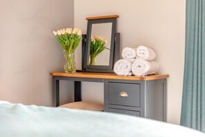Ein Schlafzimmer mit einem Bett, einem Nachttisch mit Spiegel, einer Vase mit Blumen und gerollten Handtüchern.