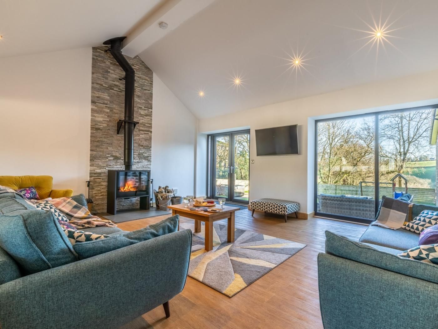 Una sala de estar moderna con chimenea, asientos cómodos, un televisor de pantalla plana y ventanas grandes.