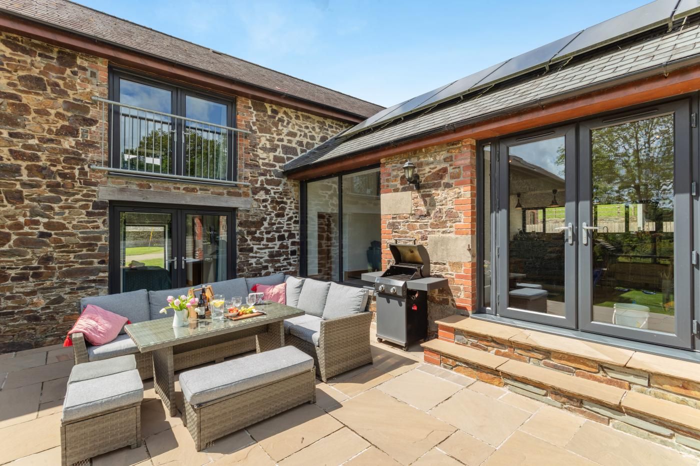 A patio area with a stone wall, a glass door, a barbecue grill, and outdoor furniture.