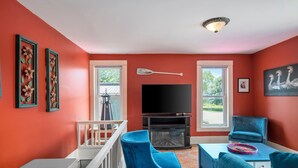 Un salon avec un téléviseur, des fauteuils bleus, une cheminée et un balcon.