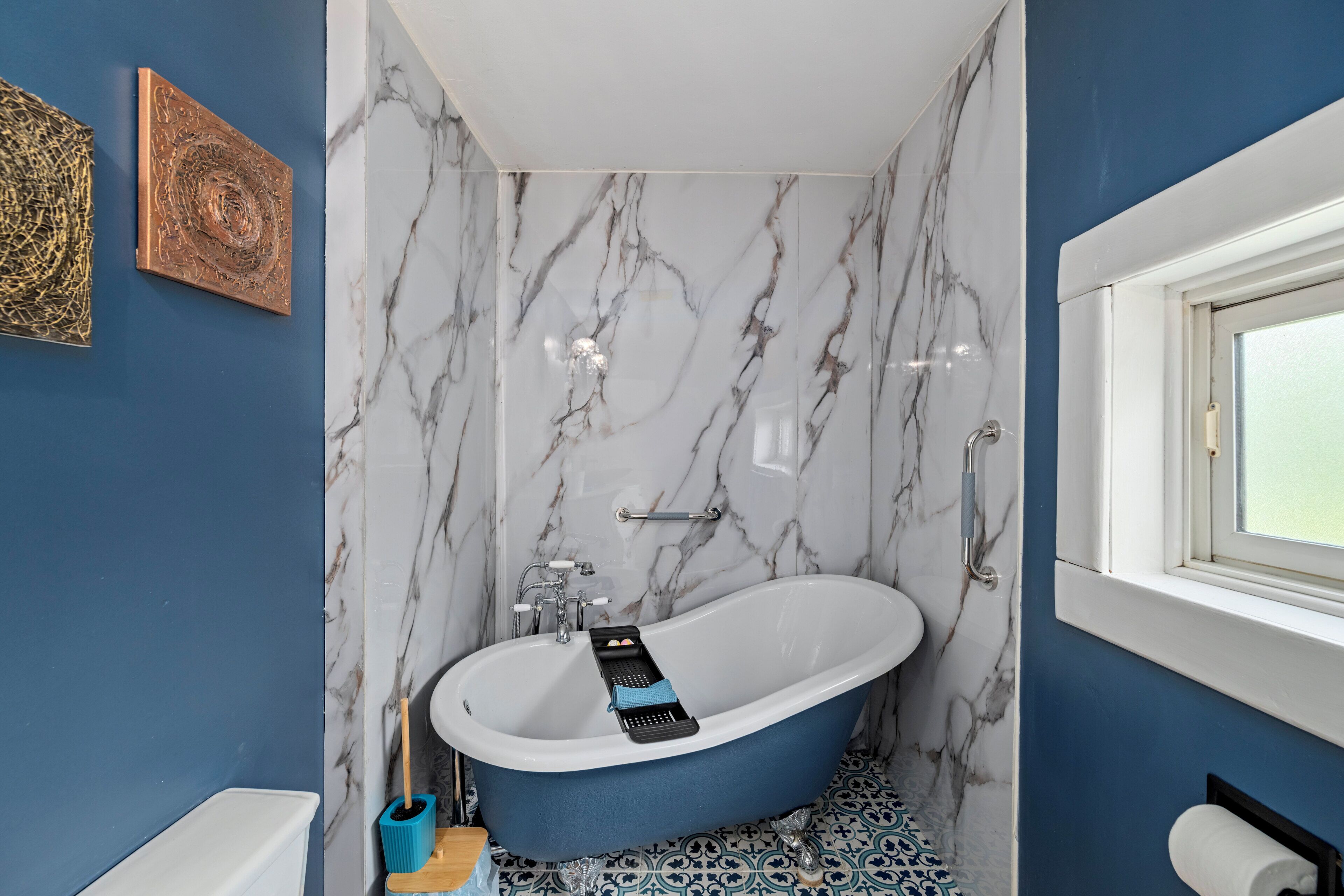 Une salle de bain avec une baignoire sur pieds, des murs en marbre, un sol bleu et une fenêtre.