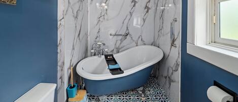 Une salle de bain avec une baignoire sur pieds, des murs en marbre, un sol bleu et une fenêtre.