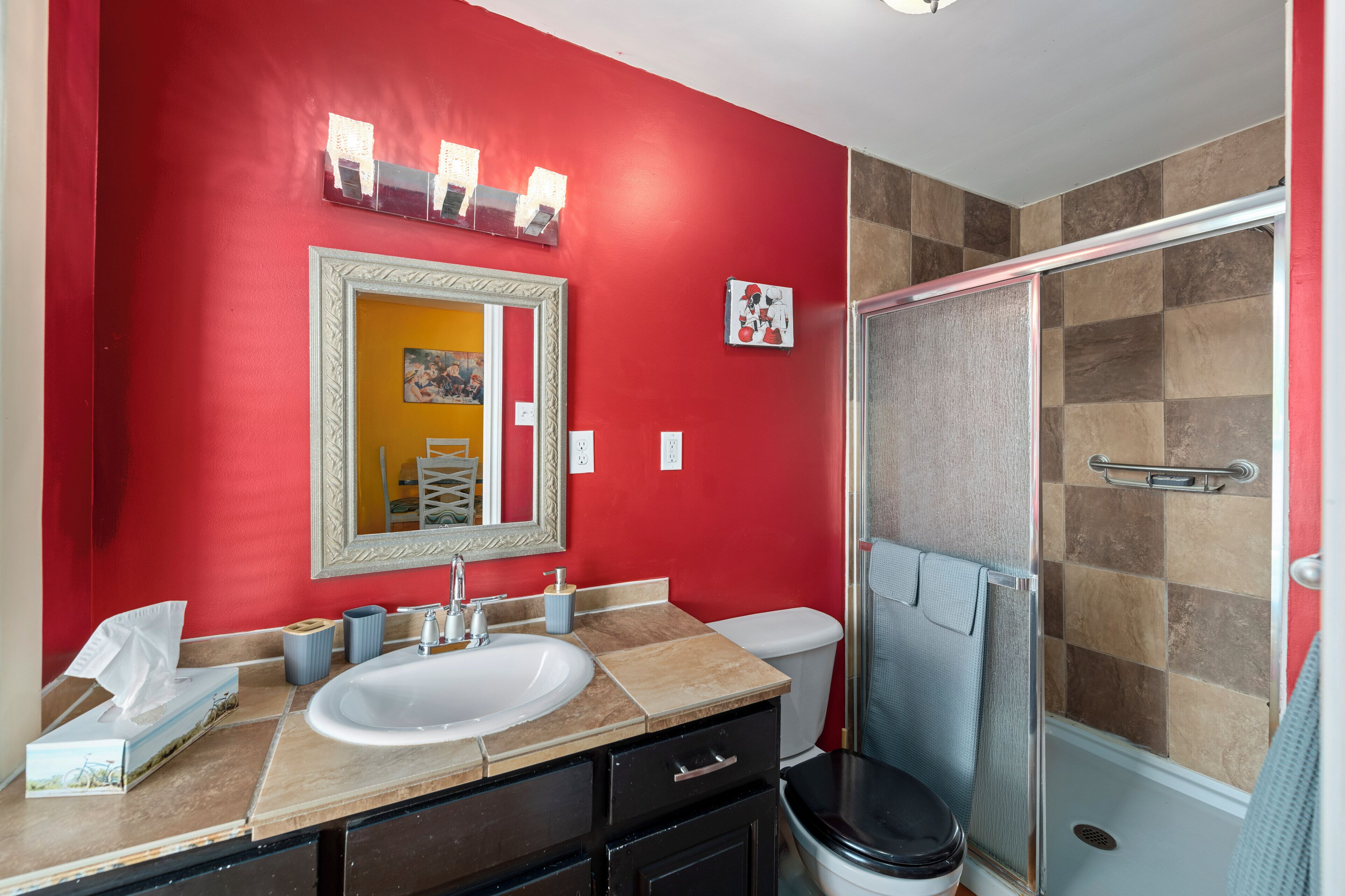 Une salle de bain avec un mur rouge, un lavabo blanc, un miroir, une douche et des toilettes.