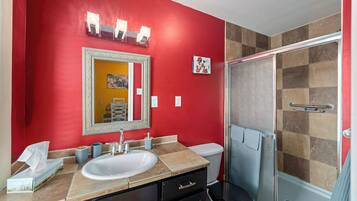 Une salle de bain avec un mur rouge, un lavabo blanc, un miroir, une douche et des toilettes.