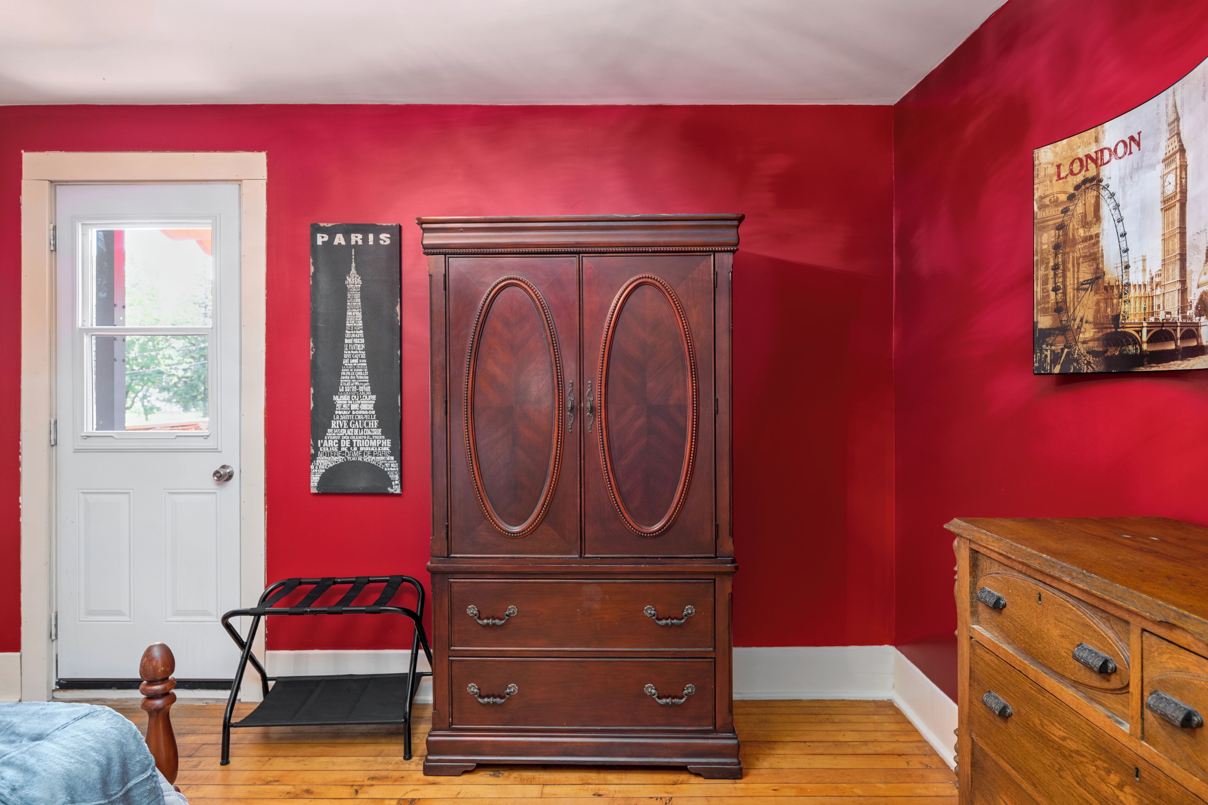 A room with a red wall, a wooden cabinet, a bench, and a door.