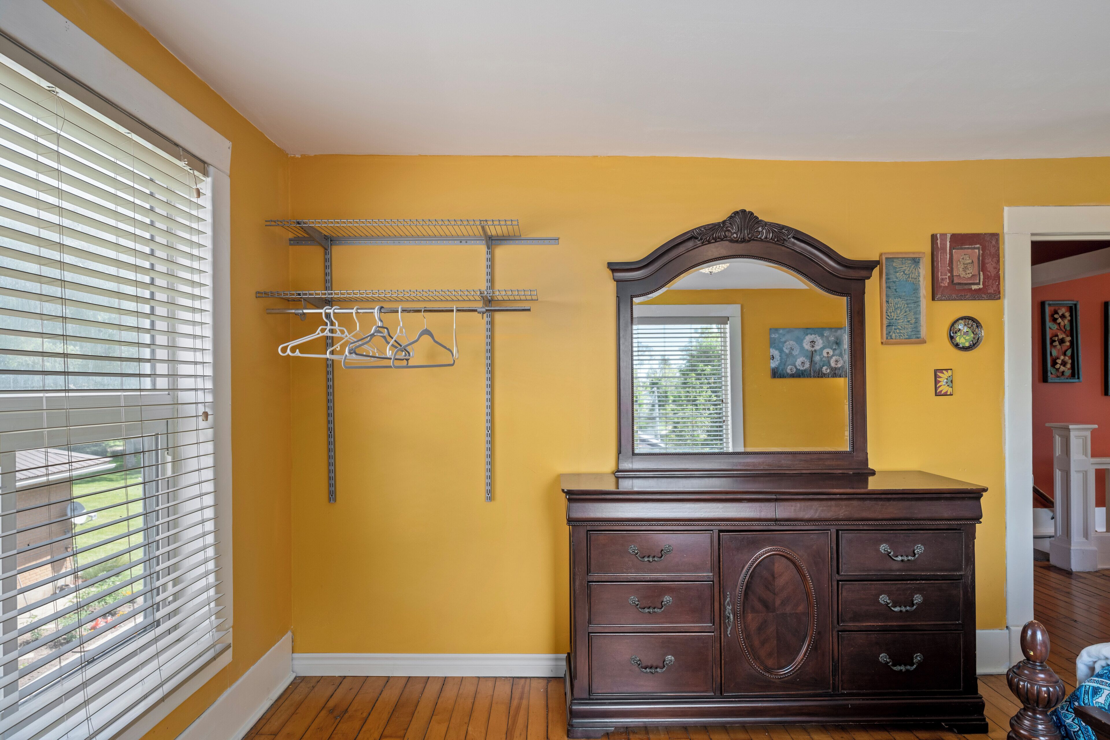 A room with a wooden dresser, a mirror, a clothes rack, and a window with blinds.