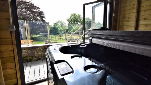 Un bain à remous dans un chalet en bois, avec une porte ouverte donnant sur un jardin.