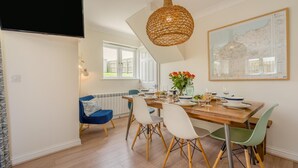 Uma área de refeições com mesa de madeira posta para quatro pessoas, cercada por cadeiras com pernas de madeira.