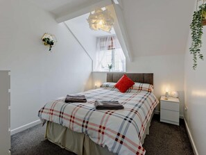 Une chambre à coucher comprenant un lit, une table de chevet, une fenêtre avec des rideaux, une plante et un luminaire au plafond original.