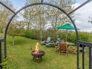 Une terrasse avec un foyer extérieur, du mobilier de jardin et un parasol vert.
