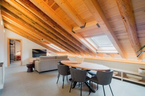 Una habitación moderna estilo loft con techo inclinado, un sofá, una mesa de comedor y sillas.