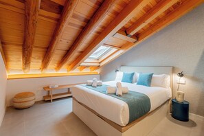 A bedroom with a large bed, a skylight, a bedside table, and a nightstand with a lamp. - Welcomer La Latina (Madrid)