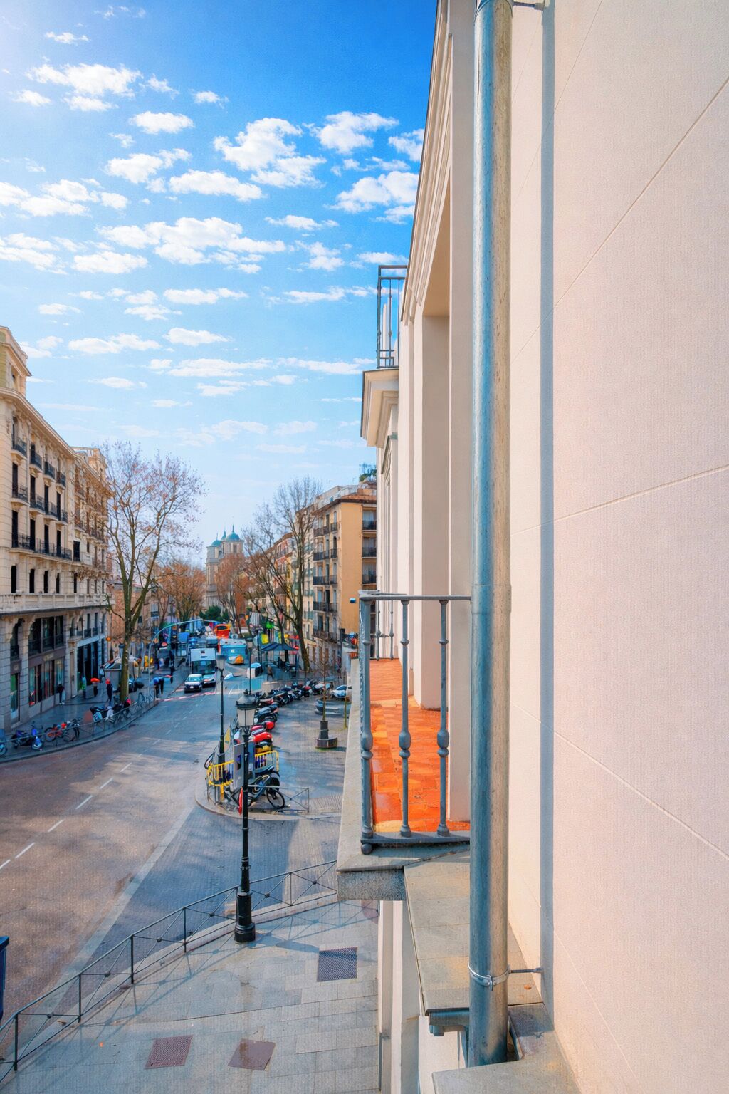 Vista de la calle con edificios, coches aparcados y cielo despejado.