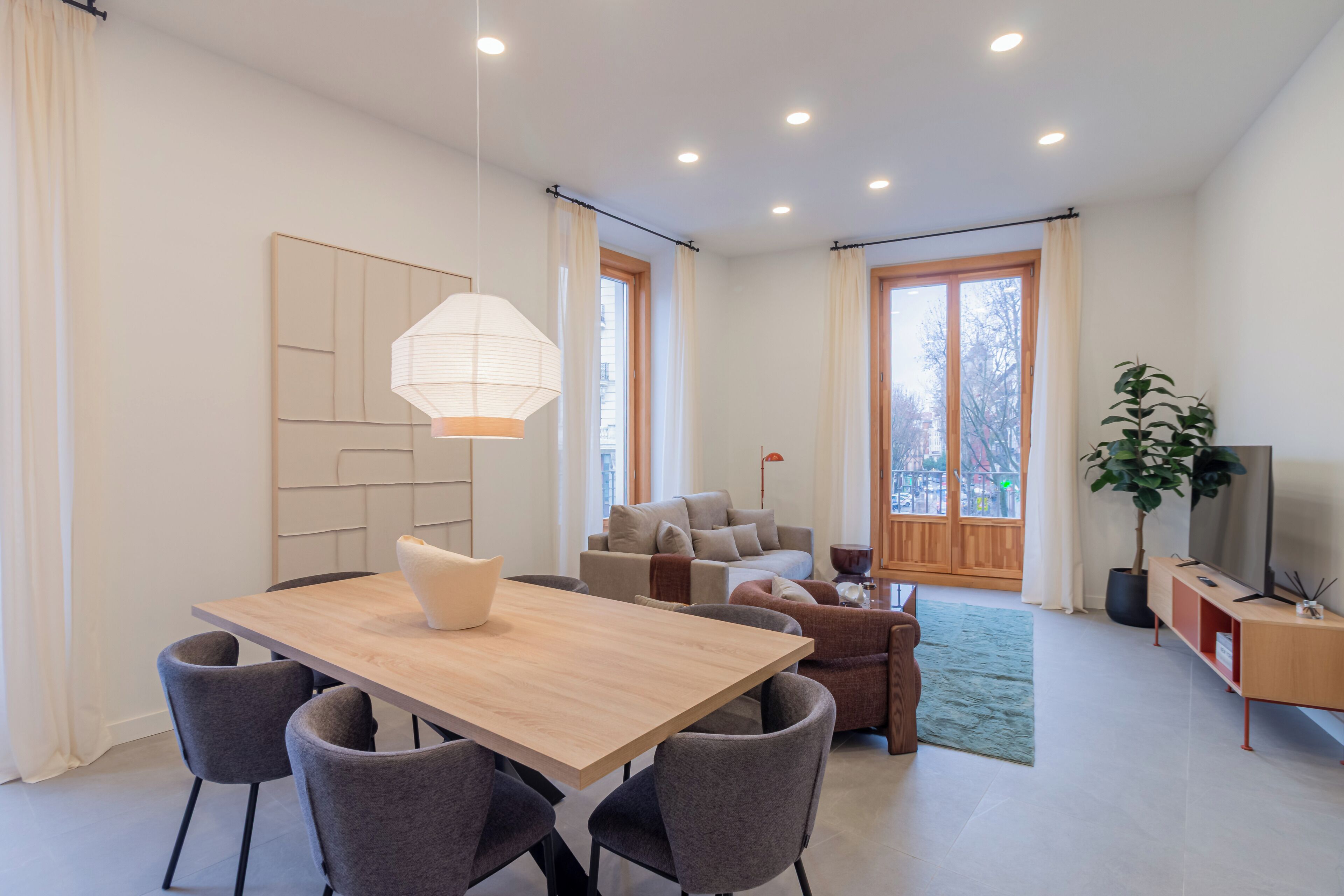 Una sala de estar moderna con comedor, un conjunto de sofás, un amplio ventanal y una planta en maceta.