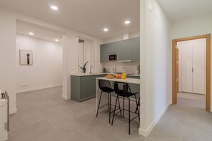 Una cocina moderna con una isla central, dos sillas tipo bar negras y un microondas sobre la isla.