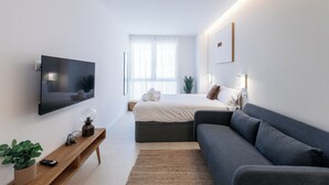 Un dormitorio moderno con cama, sofá, televisor y una planta.
