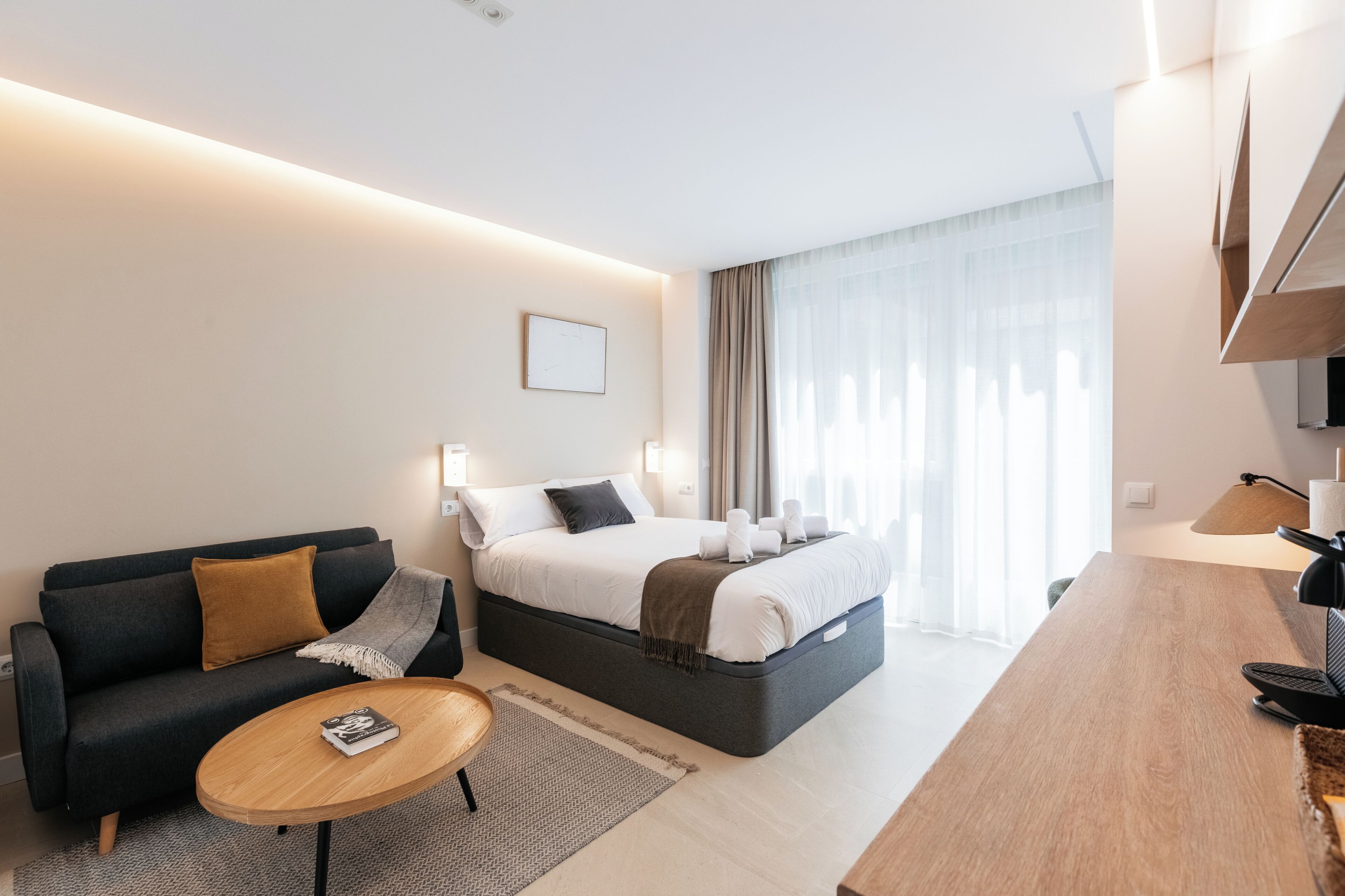 A modern hotel room with a bed, a sofa, a desk, and a lamp.