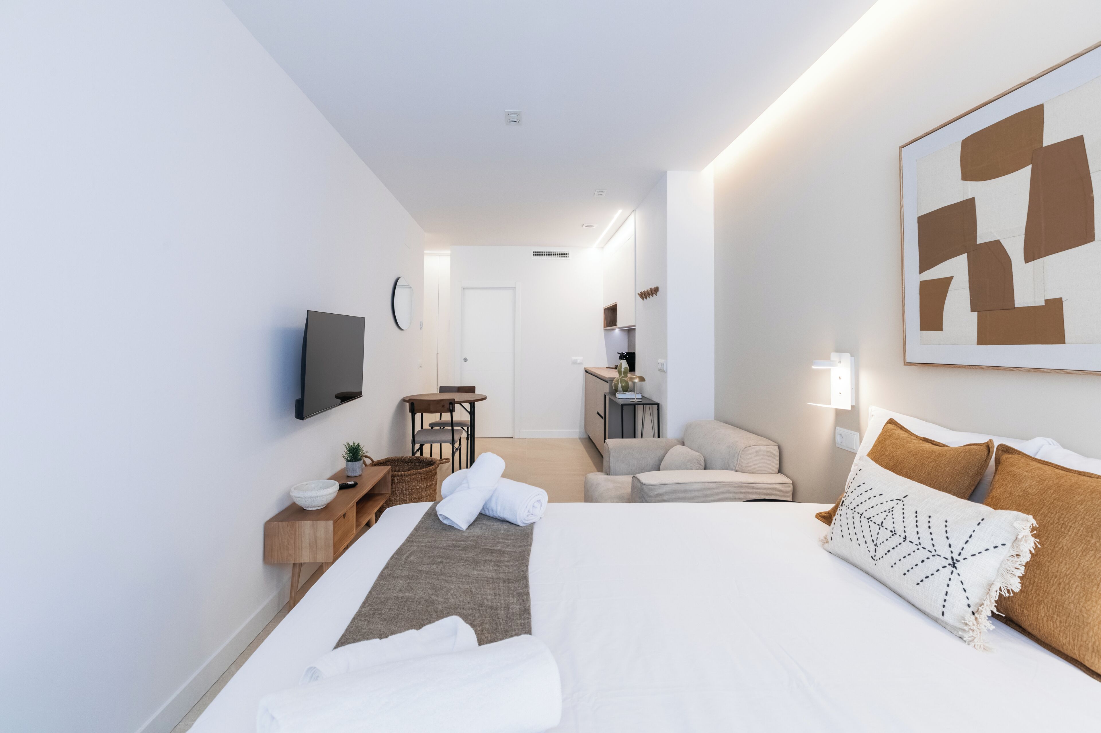 A modern hotel room with a bed, bedside table, TV, and a view of the hallway.