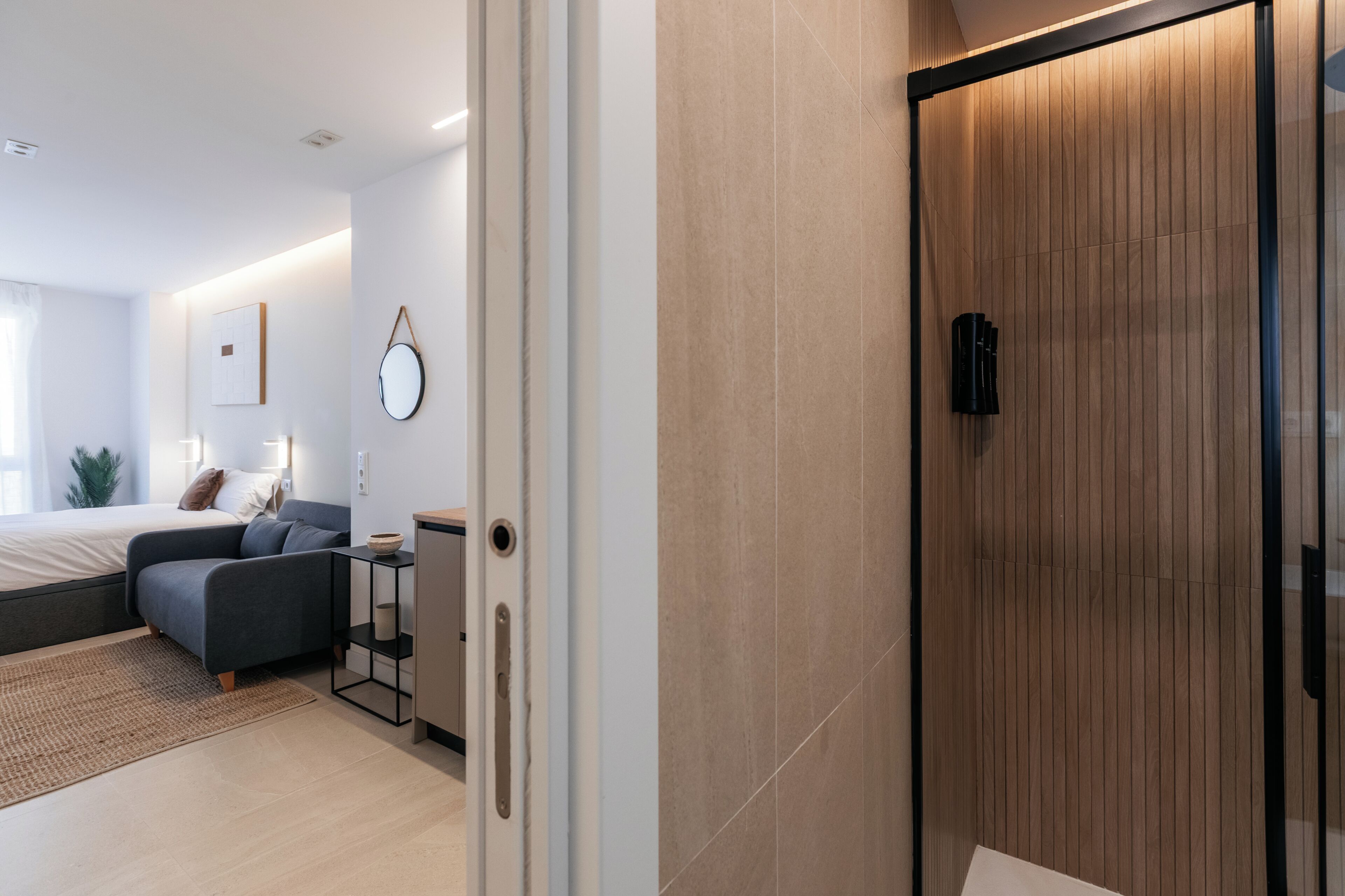 A modern bedroom with a bed, a sofa, a bedside table, and a mirror.