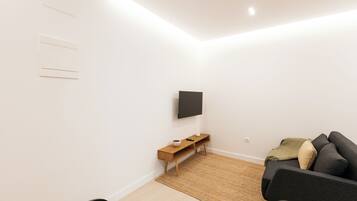 Una sala moderna con un televisor de pantalla plana montado en la pared, un mueble bajo de madera, un sofá de color oscuro y una alfombra tejida en el suelo.