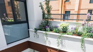 Un edificio residencial de varios niveles con balcones, ventanas grandes y plantas en macetas.