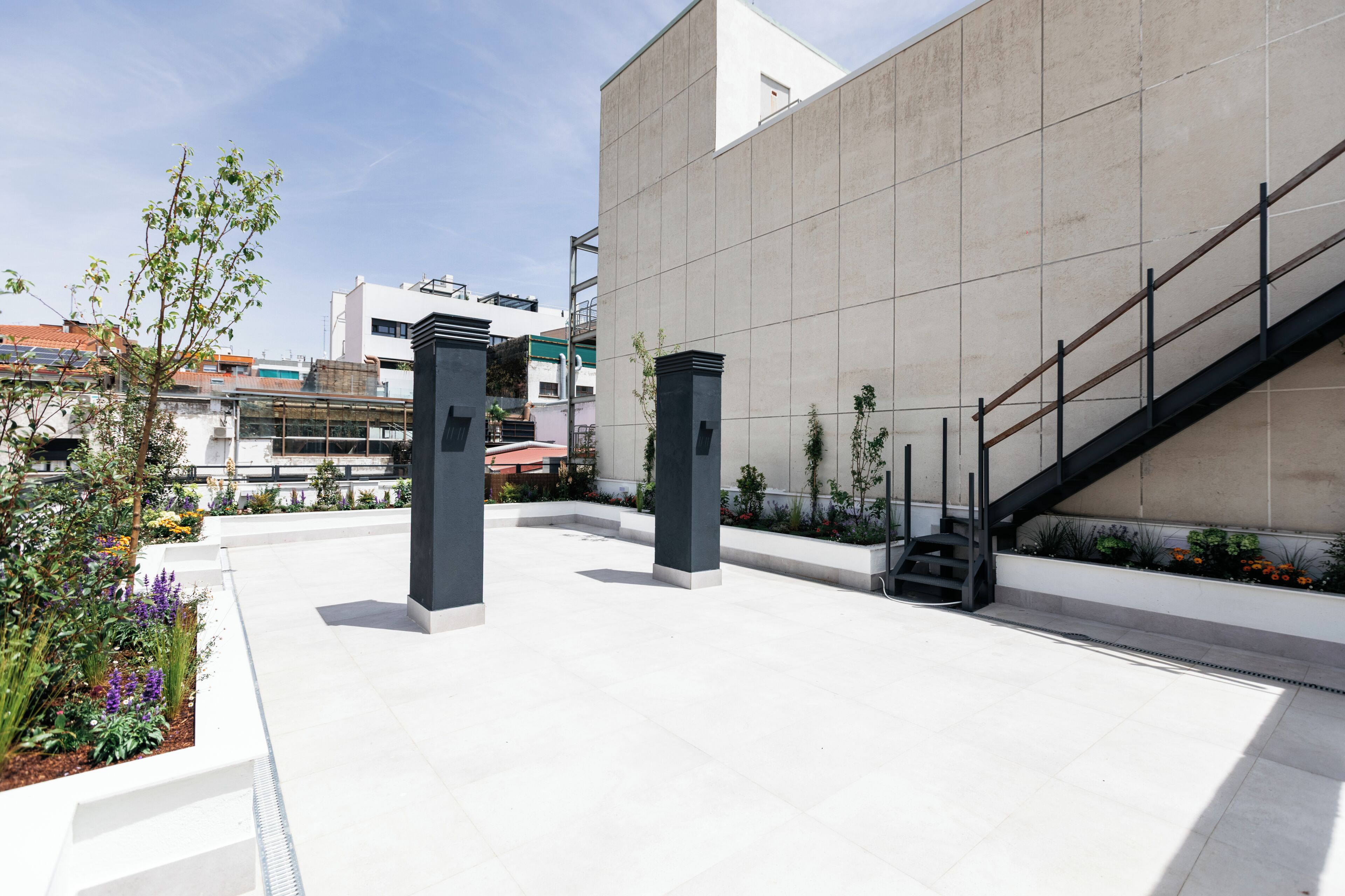 Un edificio moderno con techo plano, una escalera y un jardín con plantas y flores.