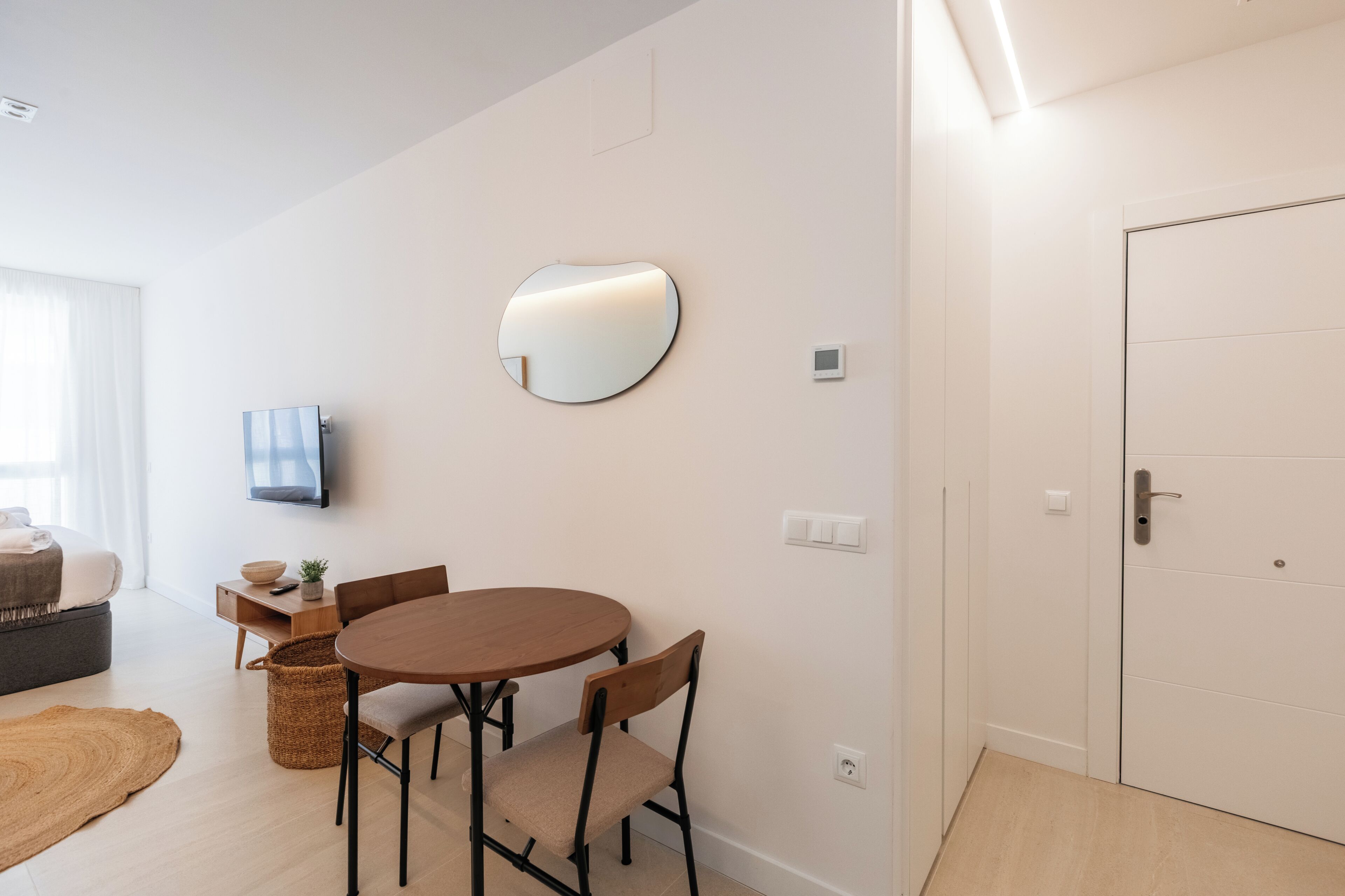 Une chambre moderne avec une table ronde, des chaises, un téléviseur à écran plat, une porte et une fenêtre avec des rideaux.