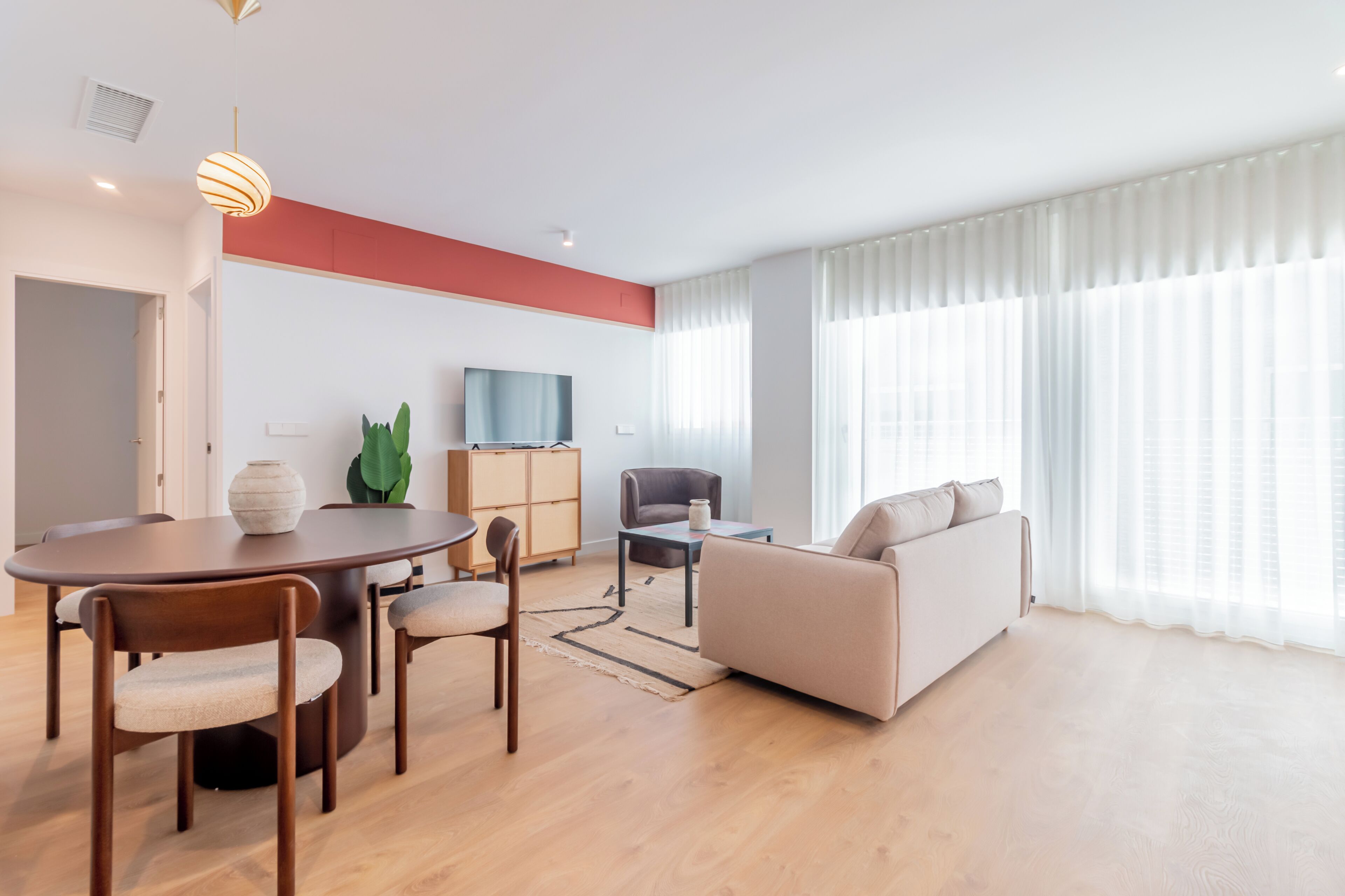 Una sala de estar moderna con comedor, sofá, televisor y un gran ventanal con cortinas.